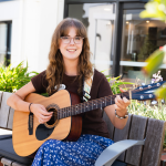 A woman sits holding a guitar