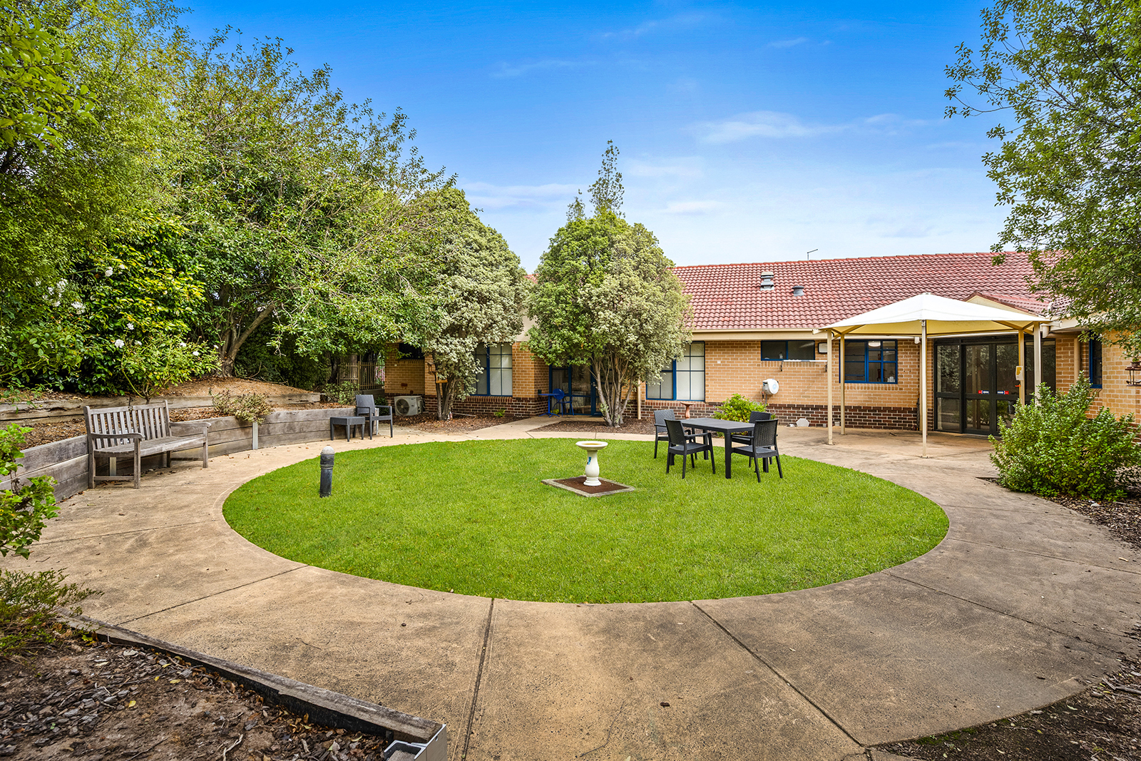 A green lawn surrounded by a circular path in front of a brick building.