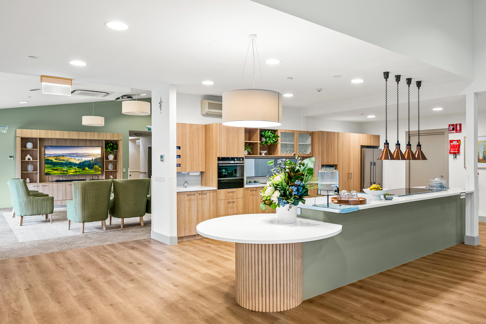 A large, bright kitchenette with a green bench and a living room behind the back wall.