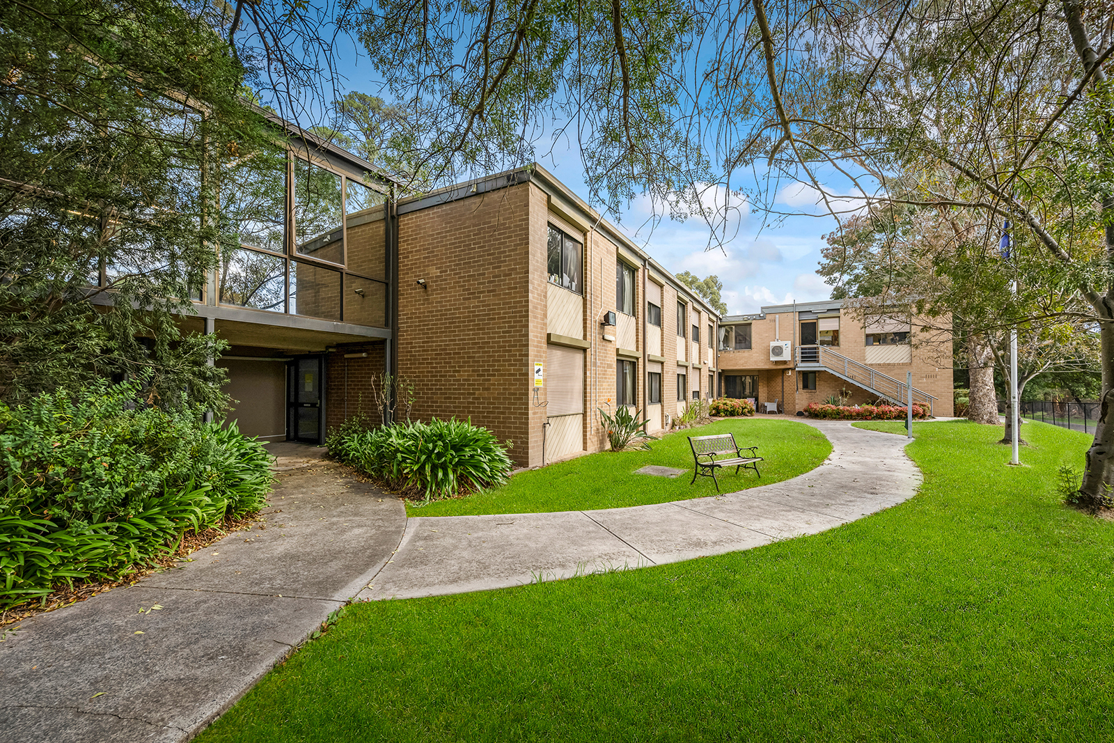 A green lawn in front of a brick double-storey building with a path cutting across it.