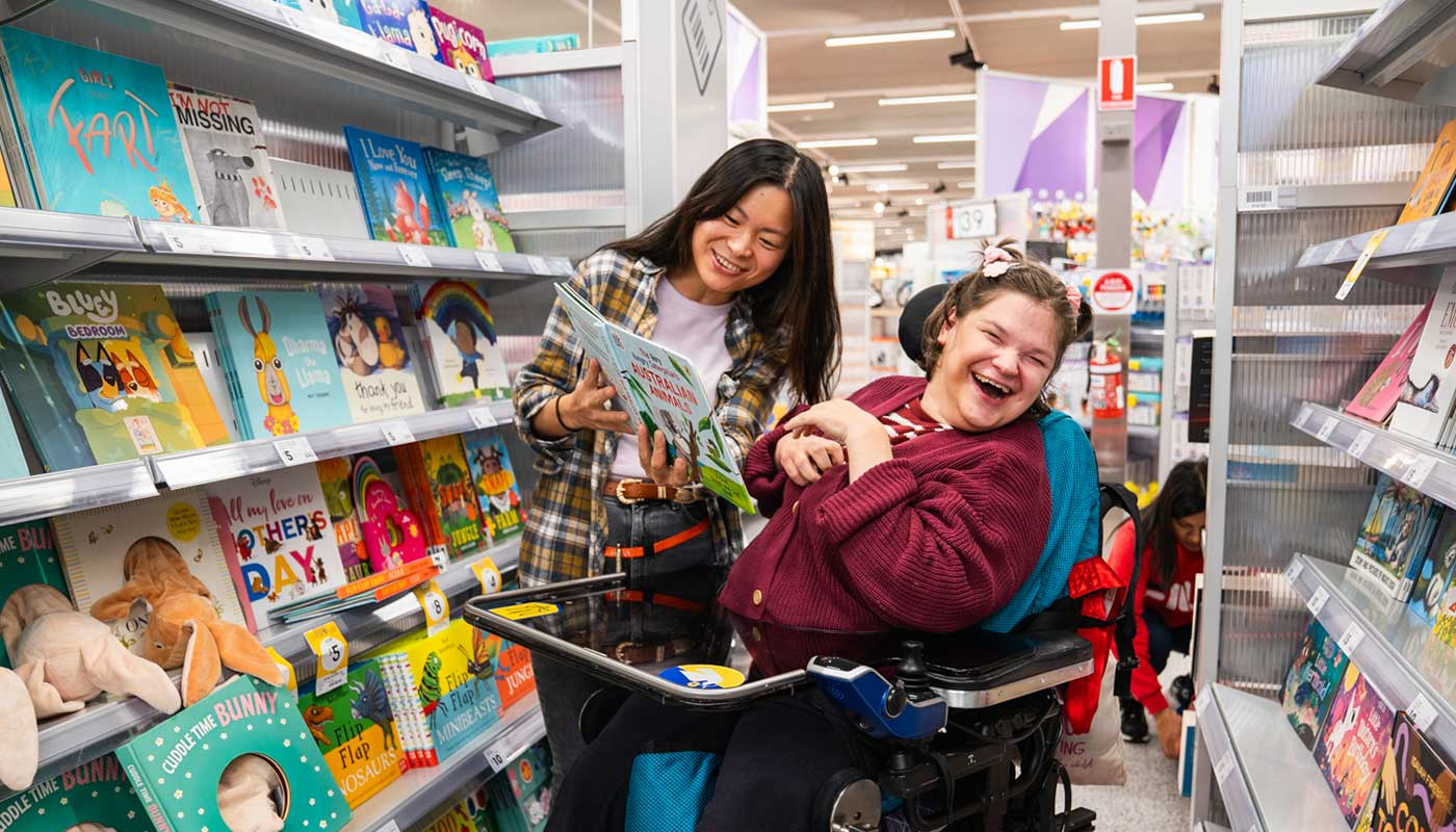 A girl in a mobility chair and a girl standing in an isle in a shop.
