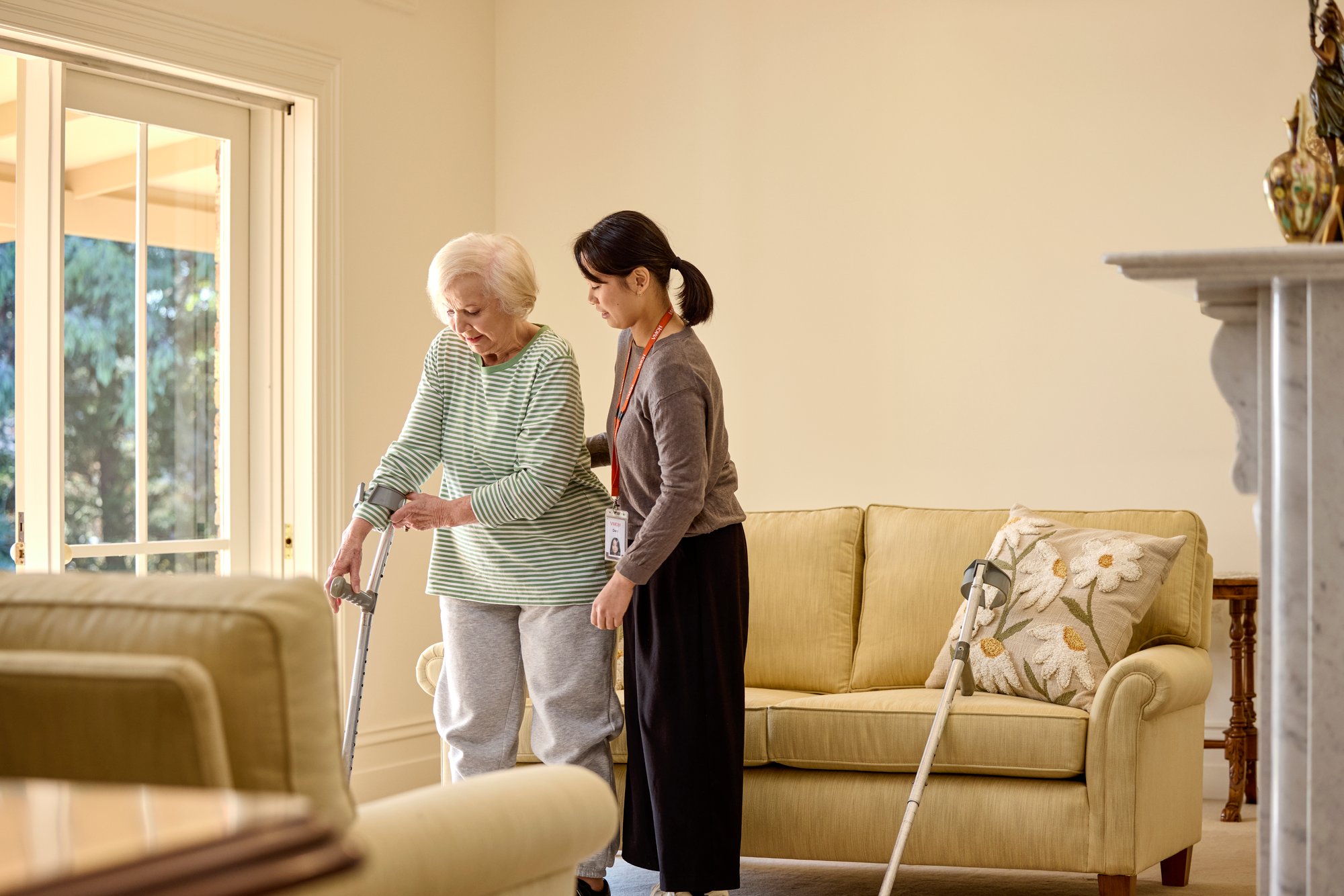 A young female allied health professional assisting an older lady with her crutches