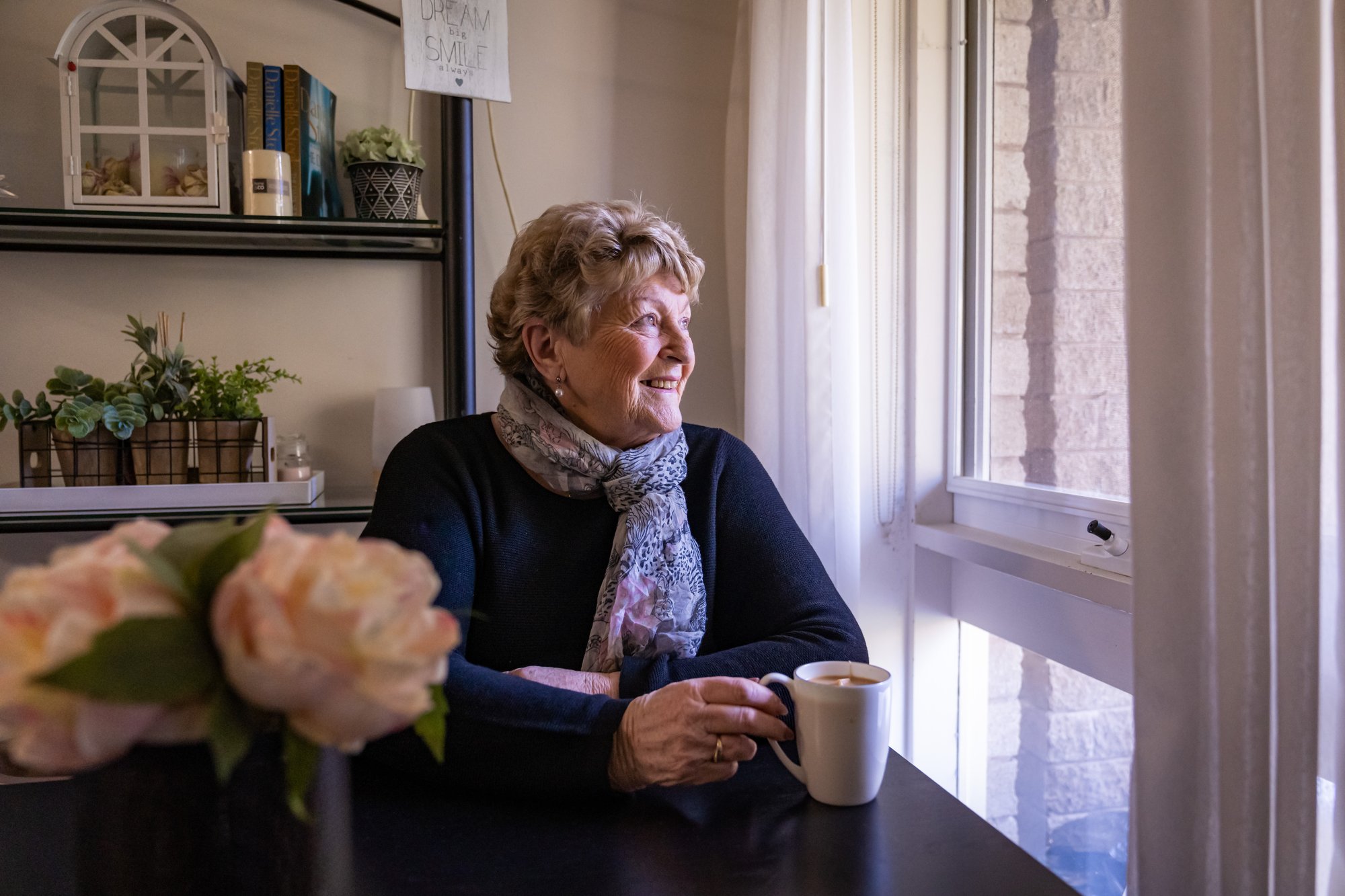A woman drinking a cup of tea and staring out the window.
