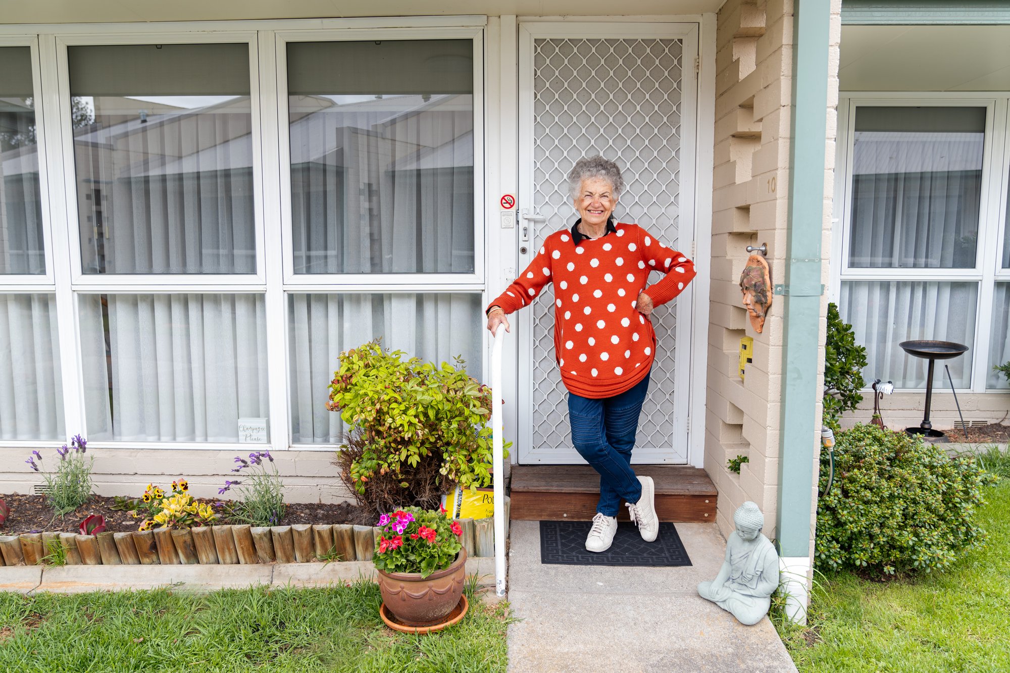 A woman in a red and white polka dot jumper standing in front of a house.
