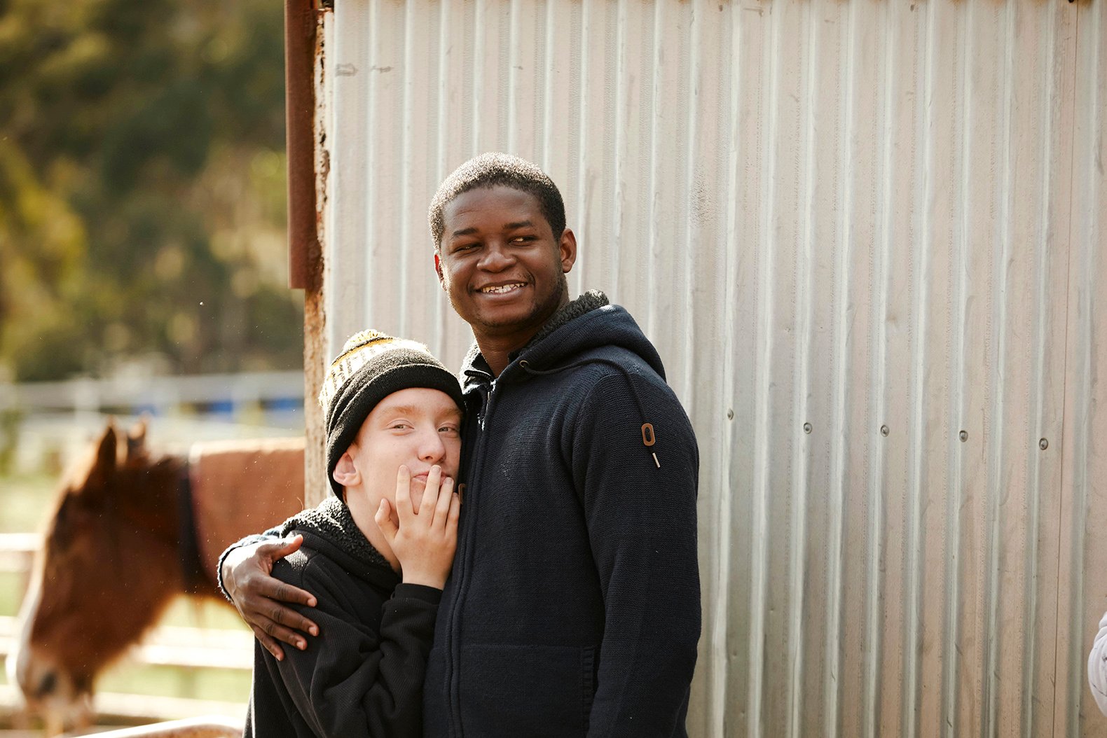 Young man hugging a teen with a horse in the background
