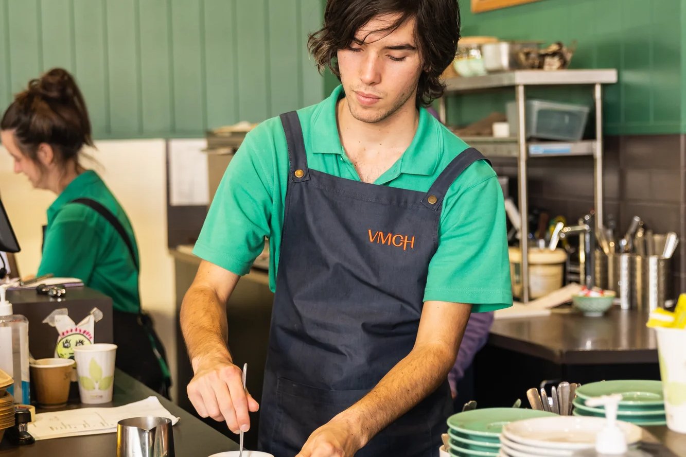 A teenage boy in a green shirt making a coffee in a cafe.