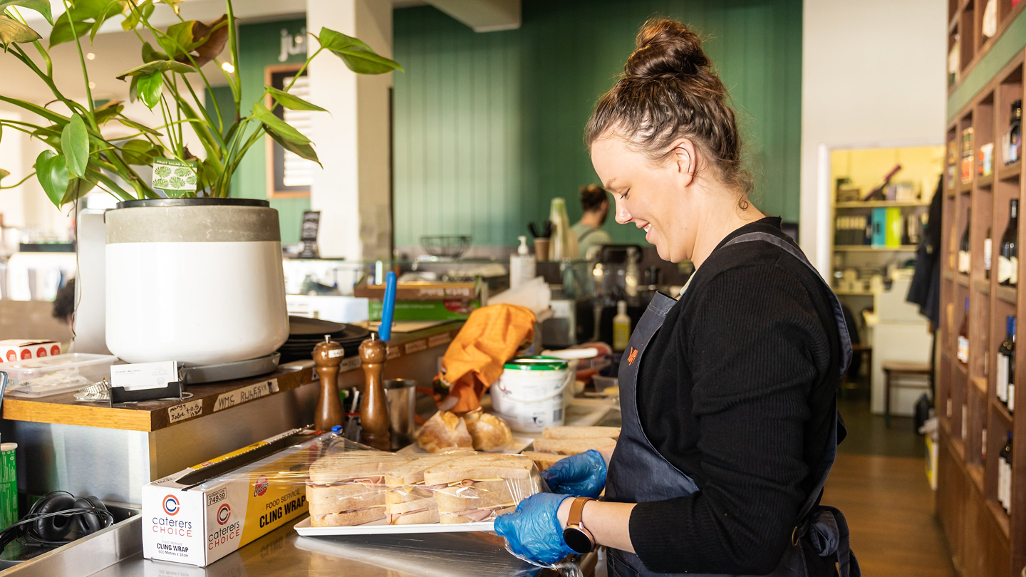 A woman standing behind a cafe counter making sandwiches.