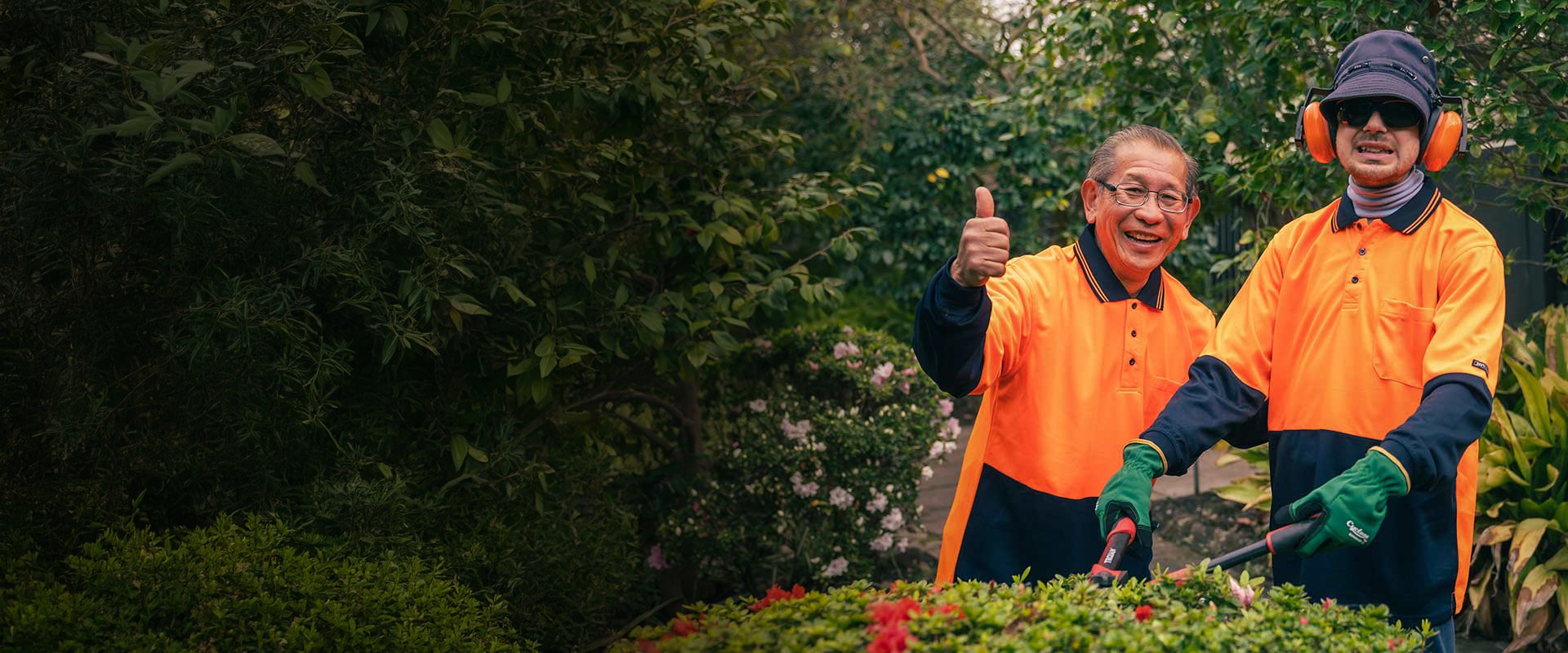 Two men in orange high-vis gardening. One man is giving a thumbs up.
