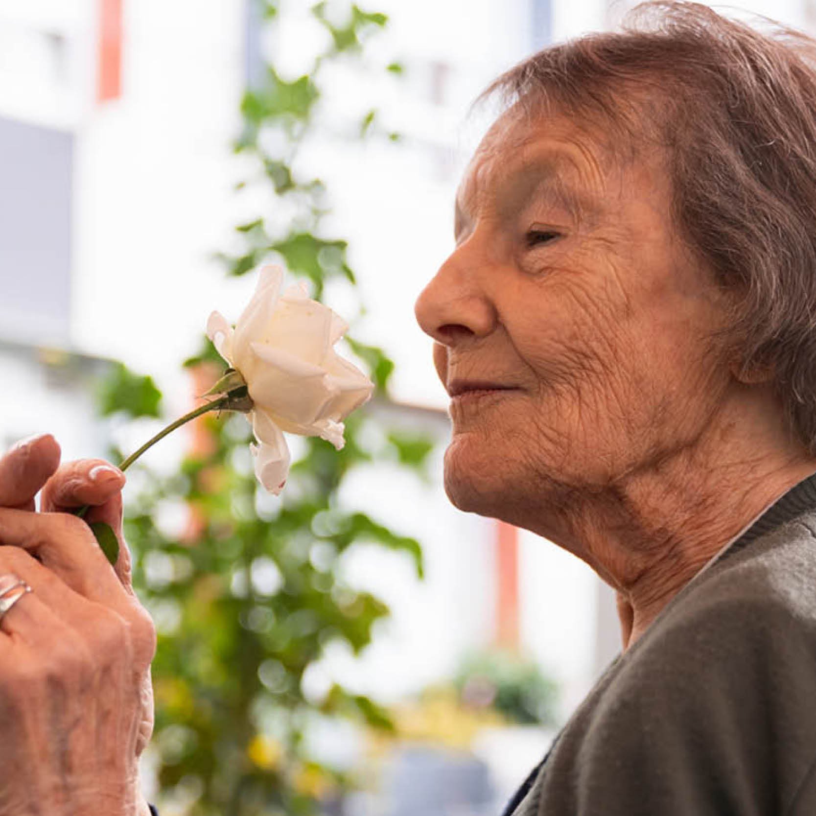 An older woman smelling a flower