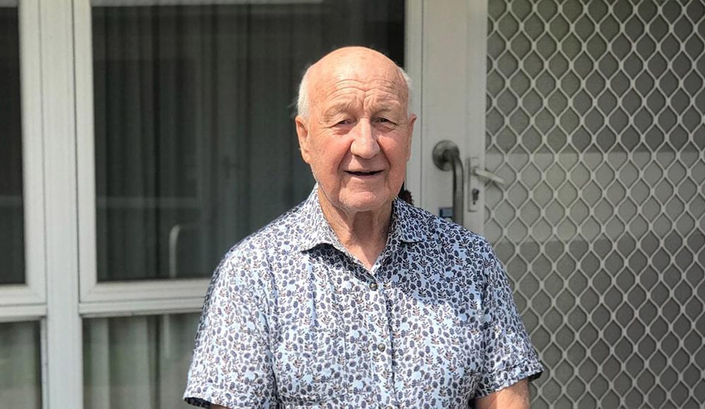 A man in a collared shirt standing in front a house.