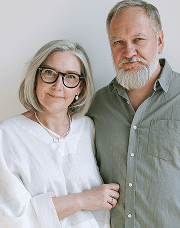 Couple smiling with mouth closed to camera, white wall in background